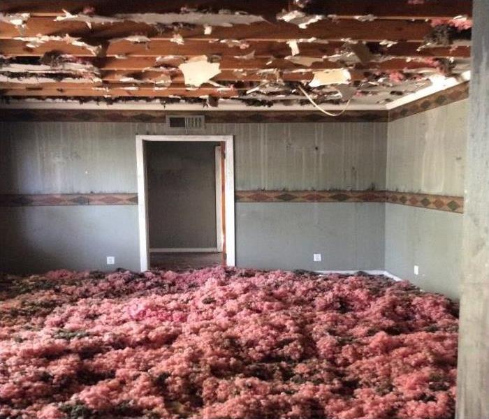 A room full of pink insulation on the floor after a fire occured. The ceiling fixtures are terribly torn. 